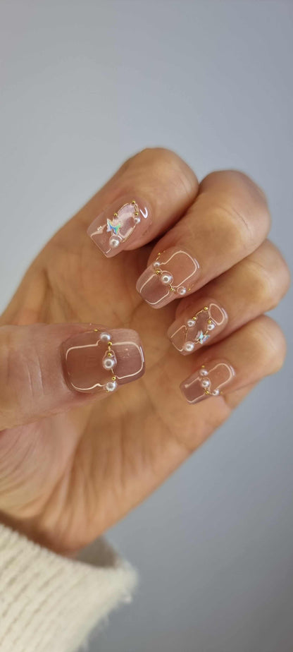  Hand wearing Khawla brown and nude press-on nails by Nail Addict, featuring elegant gold chains and pearl accents on each nail.