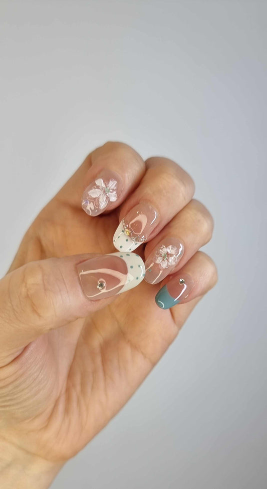 Hand wearing Layan long coffin press-on nails in sheer pink with intricate white floral lace and pearl details.
