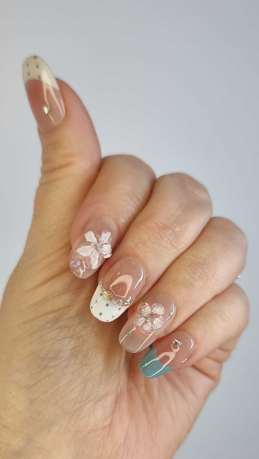 Close-up of Layan press-on nail showing the translucent pink base with a white floral design and a small pearl.