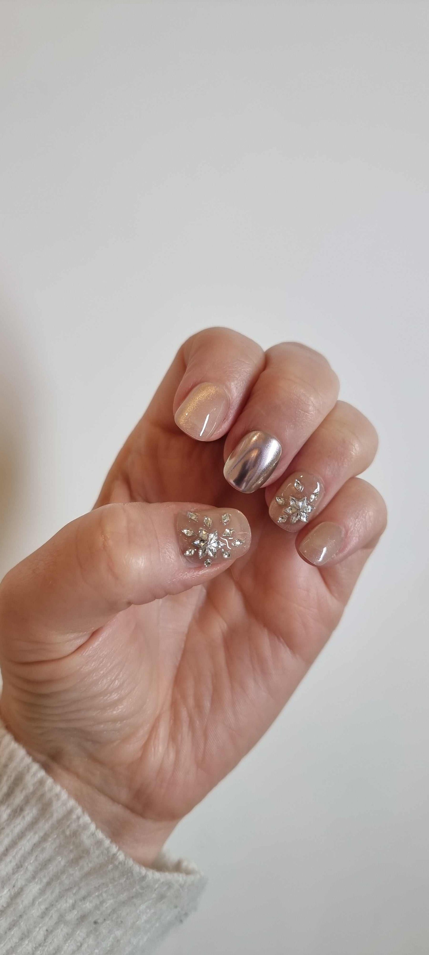 A model's hand wearing the luxurious Liwa Luxe press-on nails, showcasing the intricate 3D gem clusters and chrome finish.