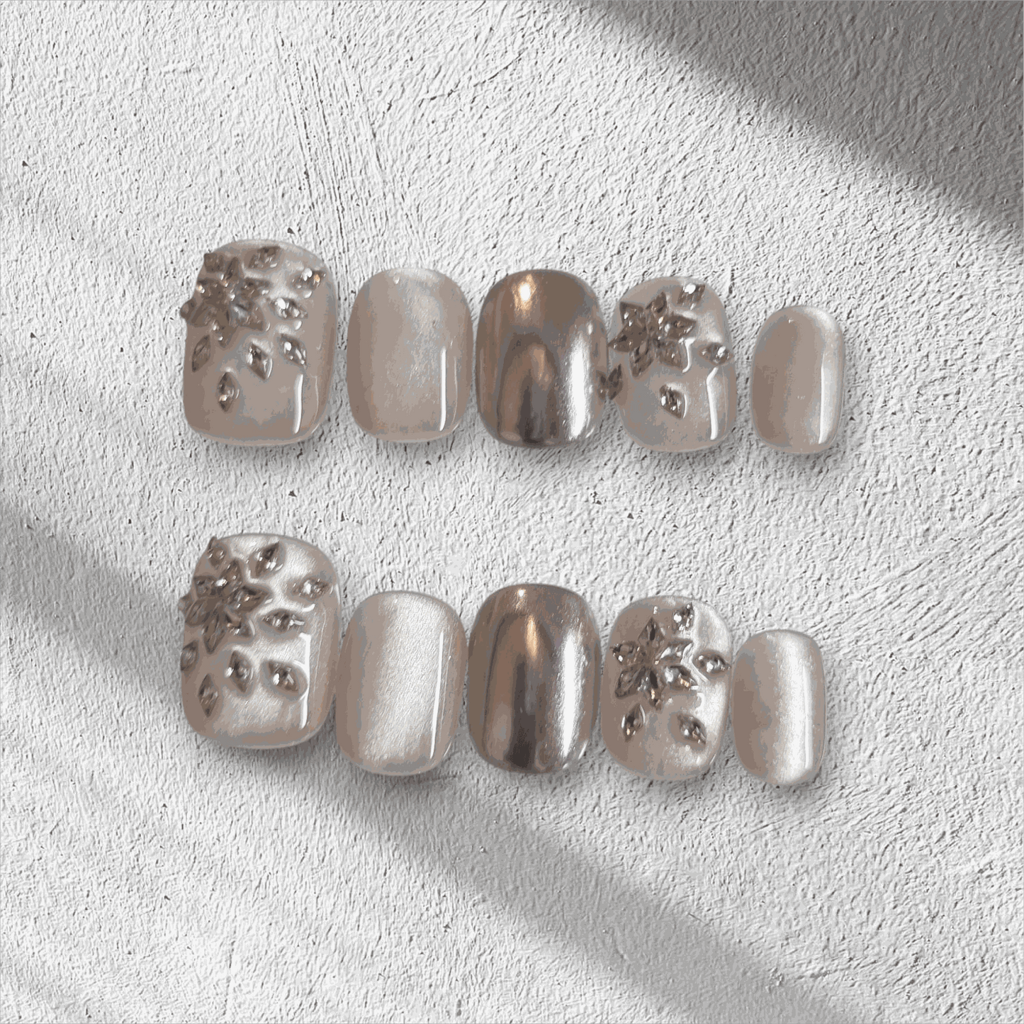The Liwa Luxe press-on nail set in a short squoval shape, featuring a mix of chrome, pearlescent, and 3D gem cluster accent nails.