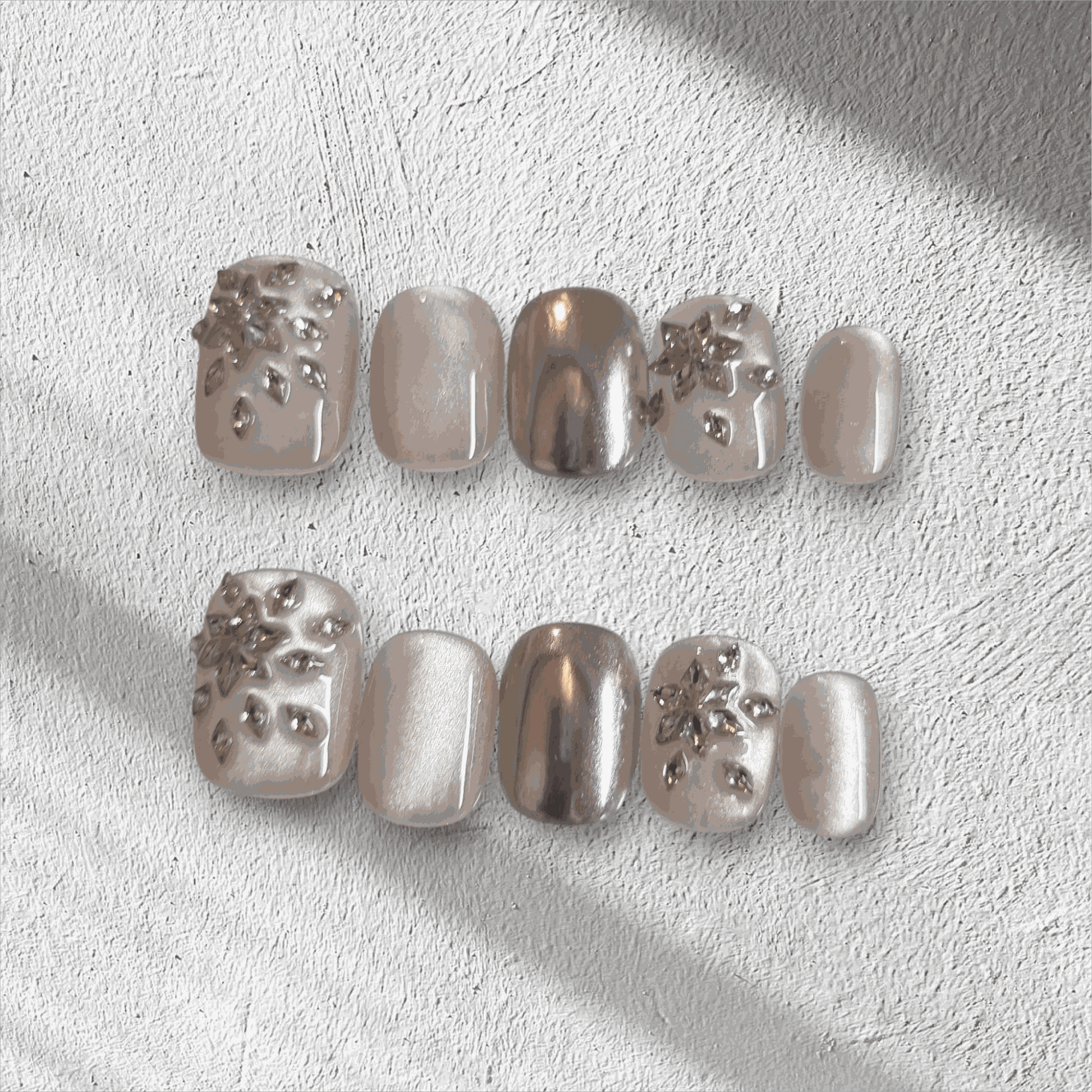 The Liwa Luxe press-on nail set in a short squoval shape, featuring a mix of chrome, pearlescent, and 3D gem cluster accent nails.