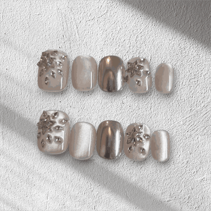 The Liwa Luxe press-on nail set in a short squoval shape, featuring a mix of chrome, pearlescent, and 3D gem cluster accent nails.