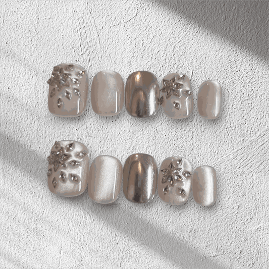 The Liwa Luxe press-on nail set in a short squoval shape, featuring a mix of chrome, pearlescent, and 3D gem cluster accent nails.