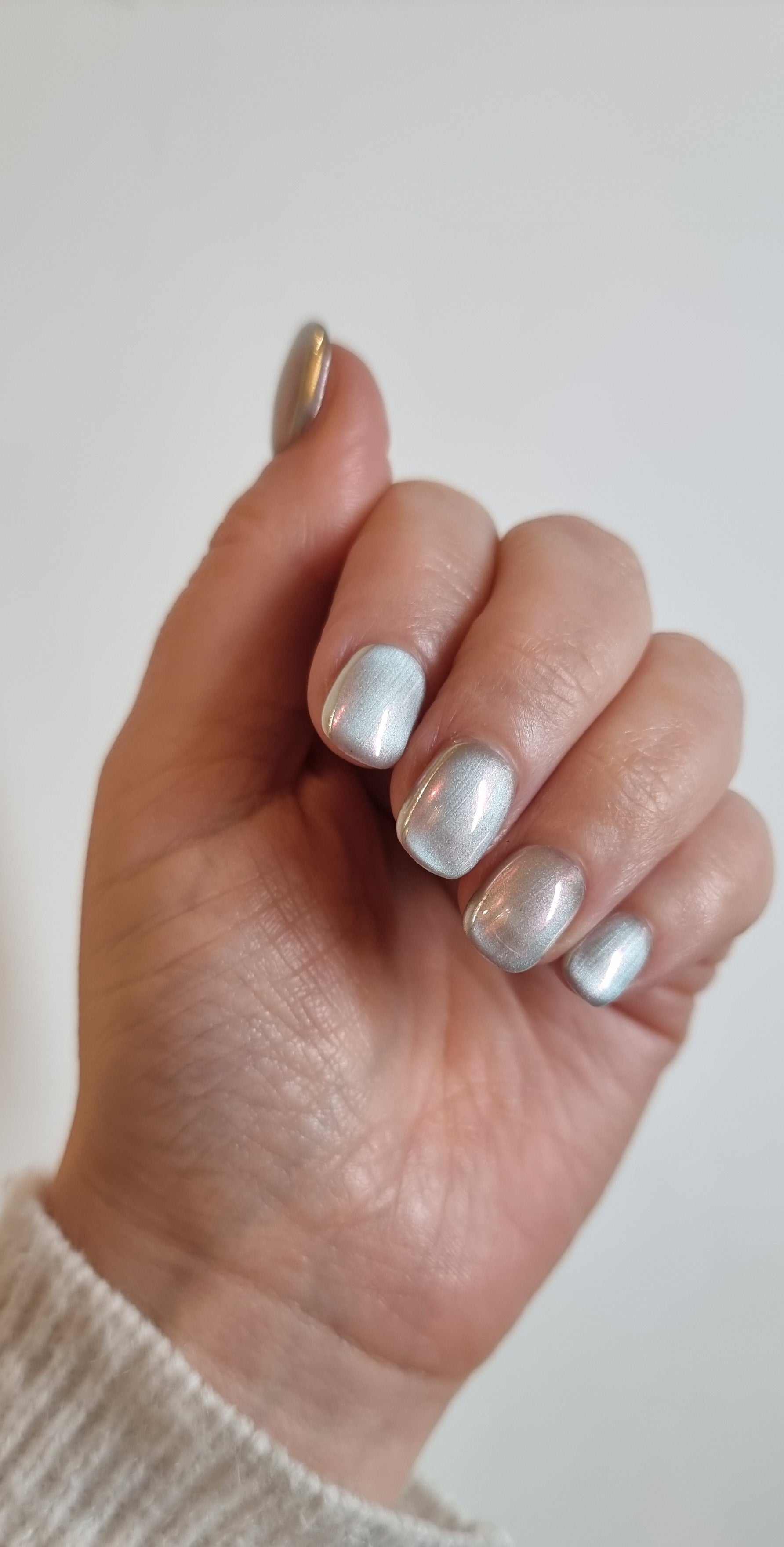 Hand wearing Lujain pearlescent gray-silver short oval press-on nails.