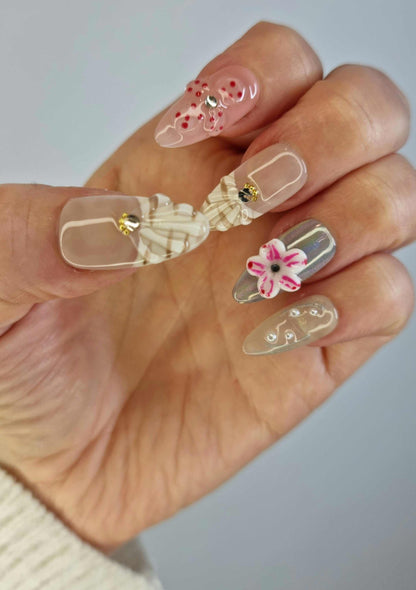 Hand wearing Madinah Majesty multi-design stiletto press-on nails with flowers, hearts, and plaid accents.