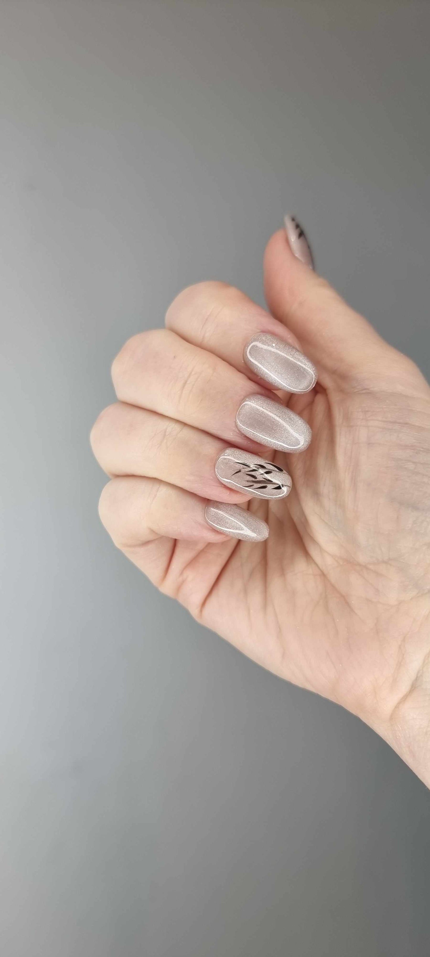 Marwa nude glitter almond press-on nails by Nail Addict, featuring a black leaf design on the middle and ring fingers