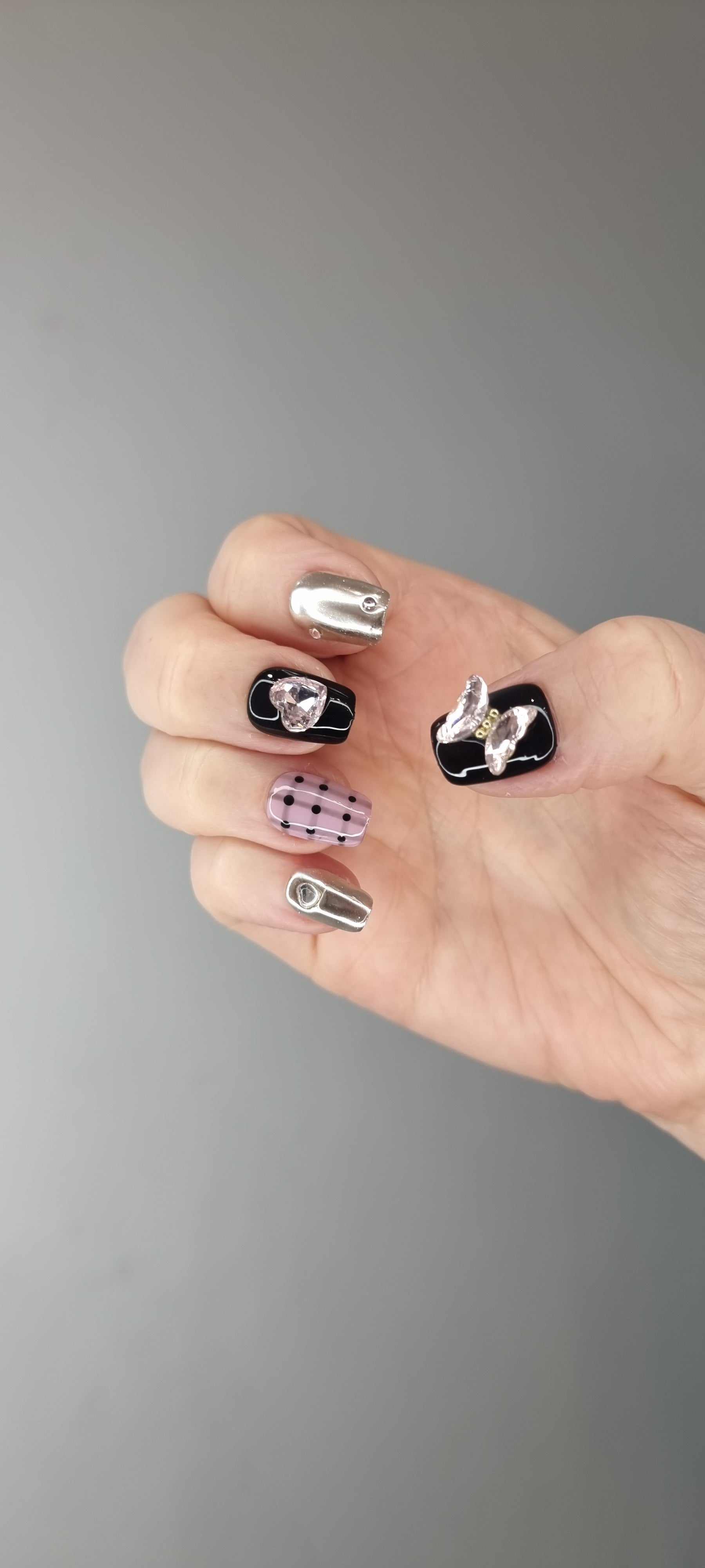 Hand wearing Maysoon coffin press-on nails in black, silver chrome, pink plaid, and polka dots.