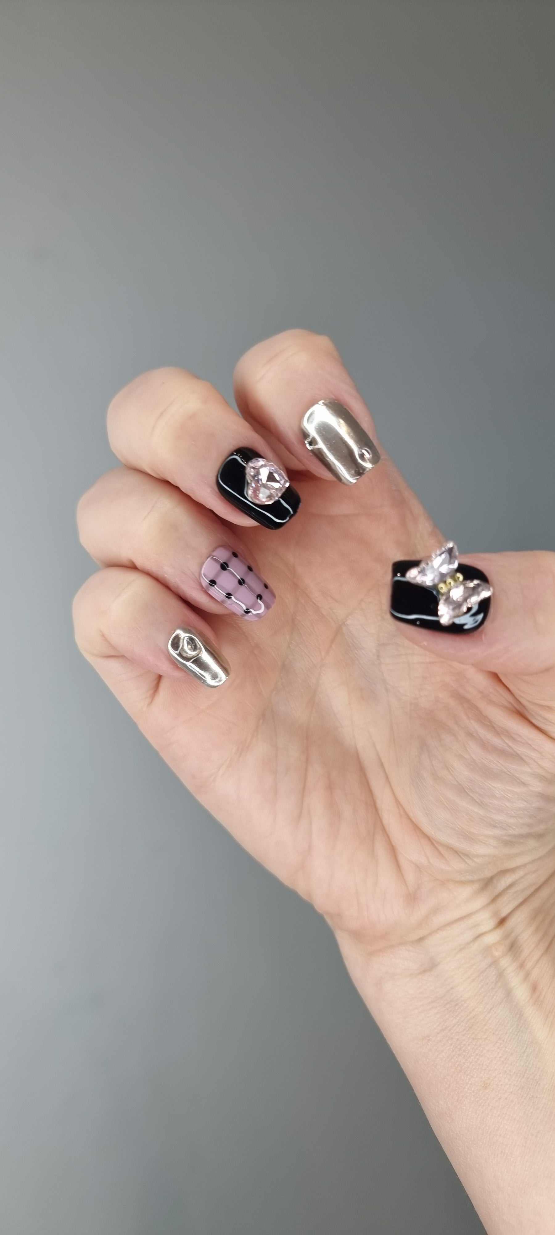 Hand wearing Maysoon coffin press-on nails in black, silver chrome, pink plaid, and polka dots.