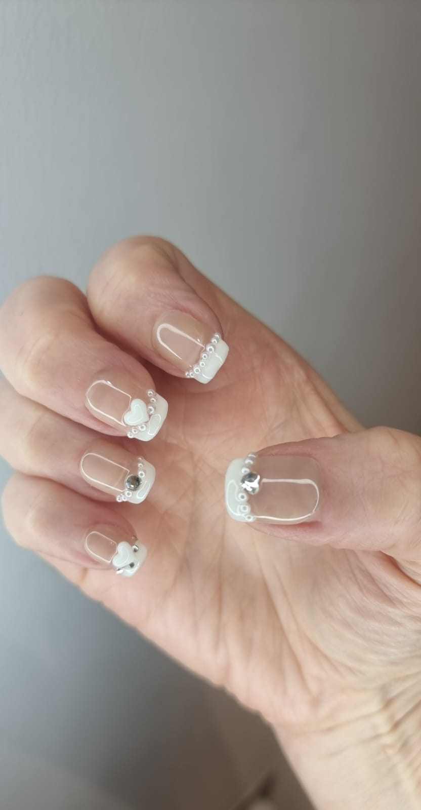 A model's hand wearing the Burj Beauty French manicure press-on nails, showcasing the elegant rhinestone detail.