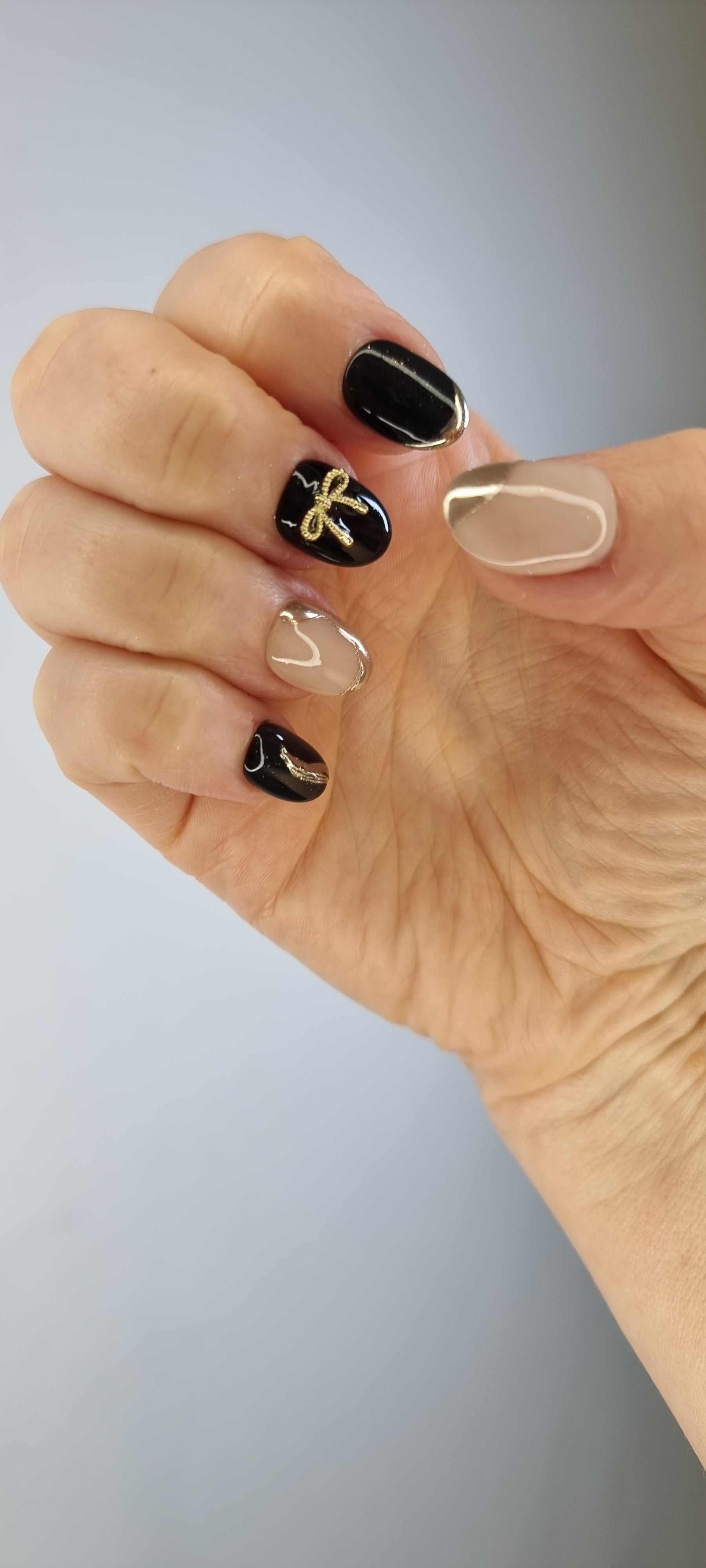 Close-up of Muscat Mystique black and nude almond press-on nails featuring gold bow accent and metallic details.