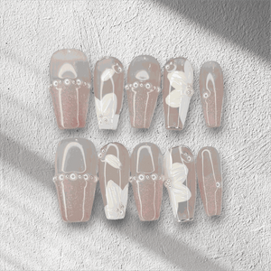 Dalia nude and brown long coffin press-on nails by Nail Addict, with a butterfly charm, pearls, and gold chain accents.