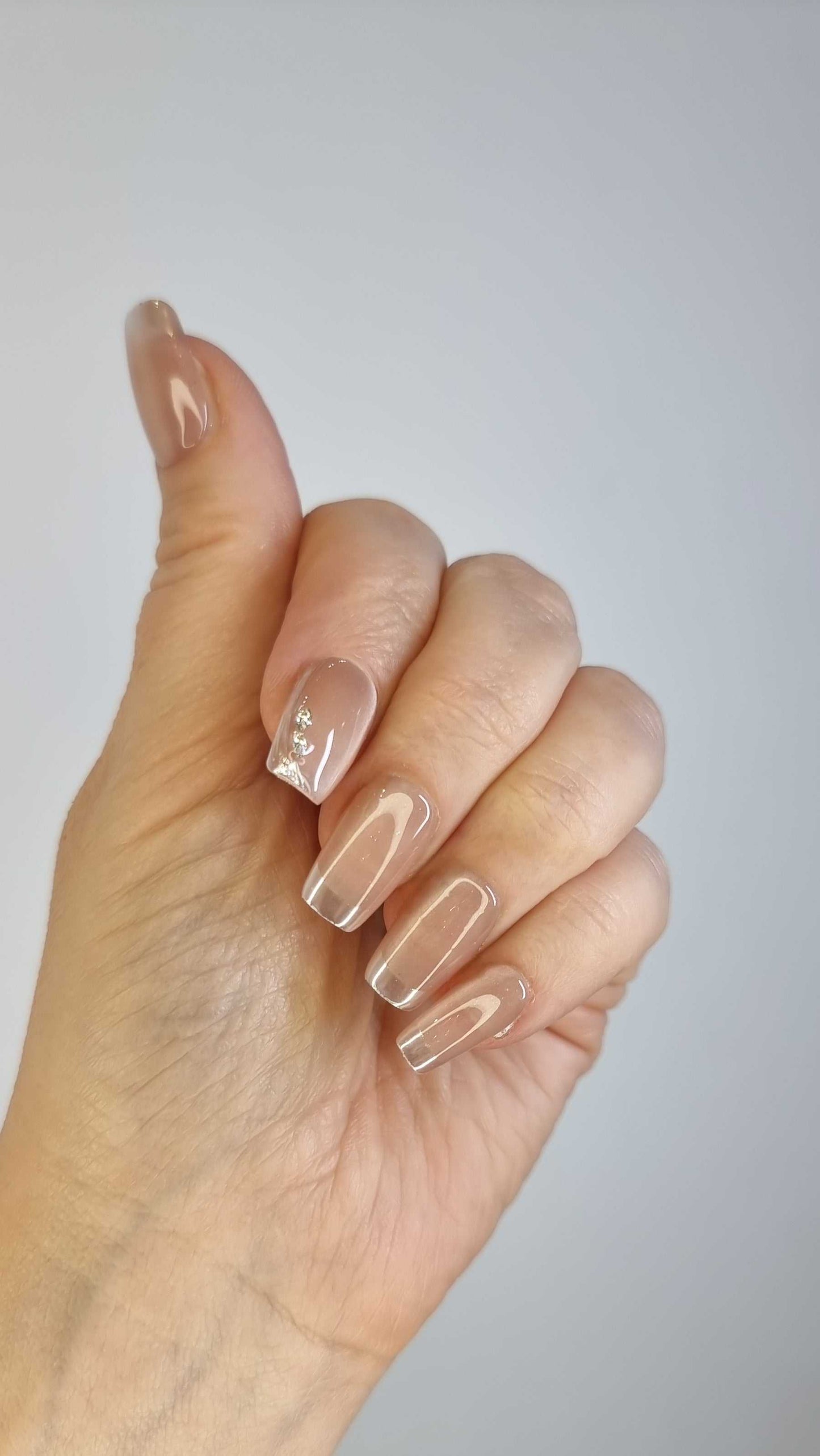 Close-up of a hand with long, almond-shaped Nahla glossy clear nude press-on nails.