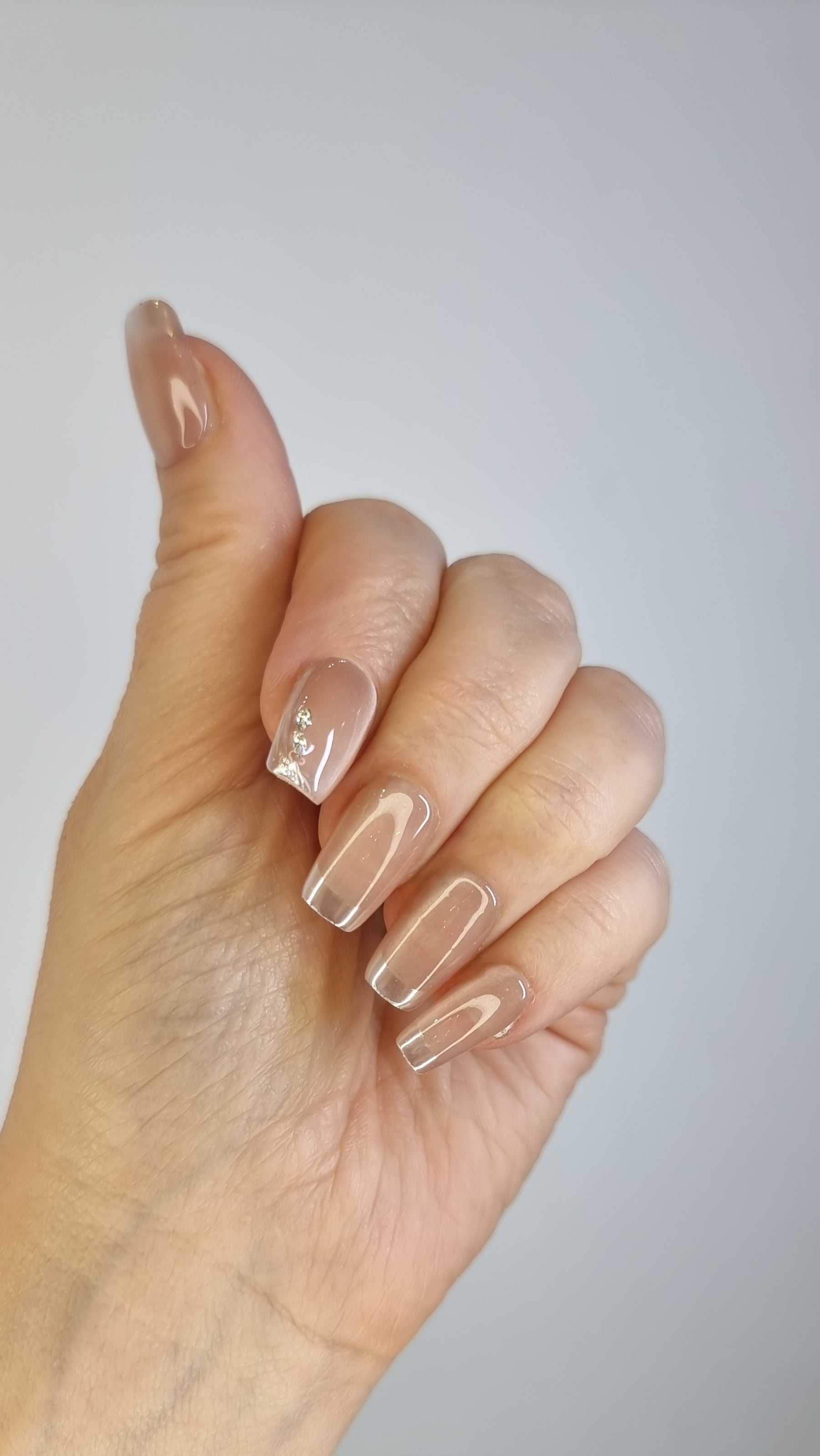 Close-up of a hand with long, almond-shaped Nahla glossy clear nude press-on nails.