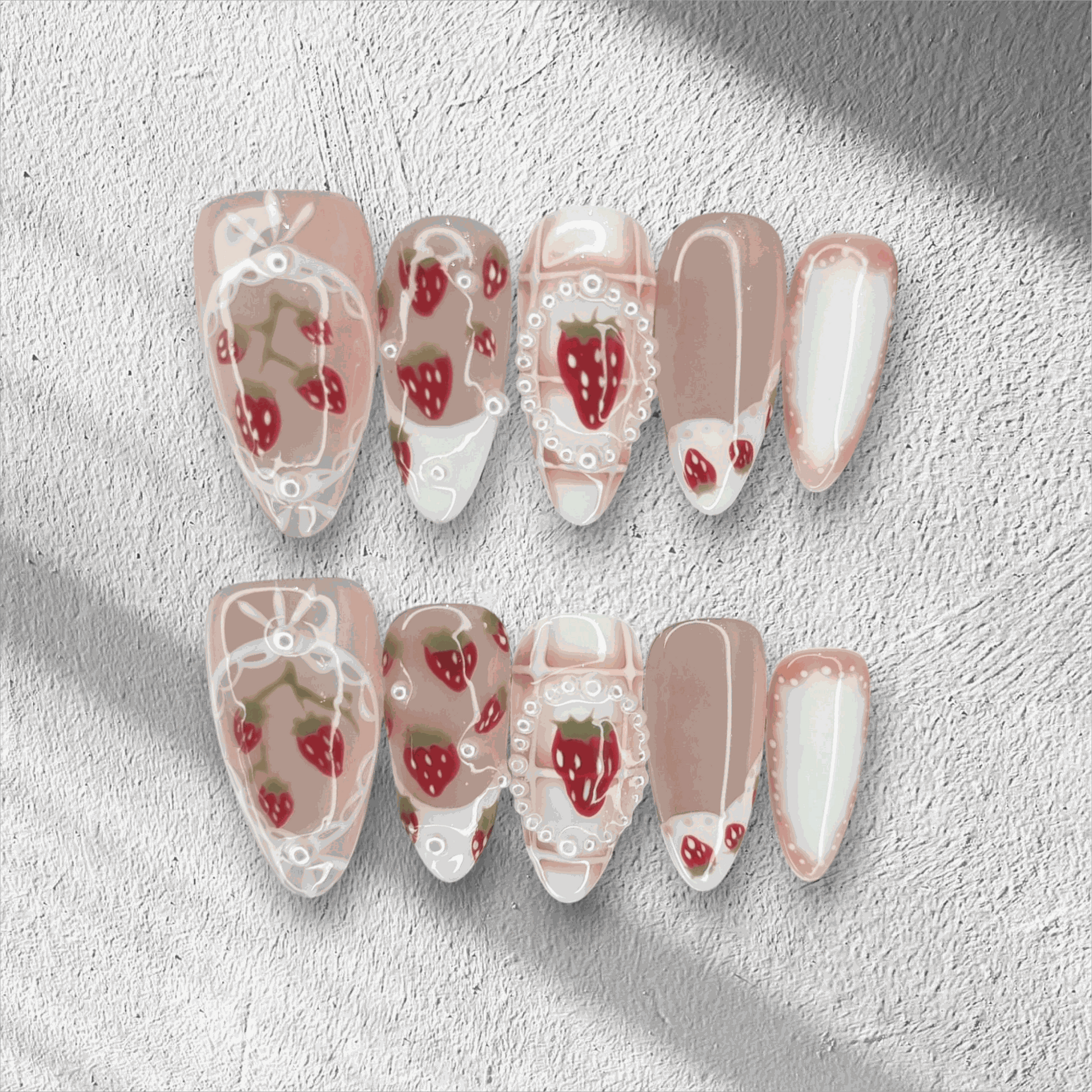 Omani Oasis press-on nails in a long almond shape, featuring a charming hand-painted strawberry design with white lace and pearl details on a nude base.