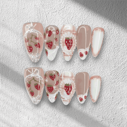 Omani Oasis press-on nails in a long almond shape, featuring a charming hand-painted strawberry design with white lace and pearl details on a nude base.