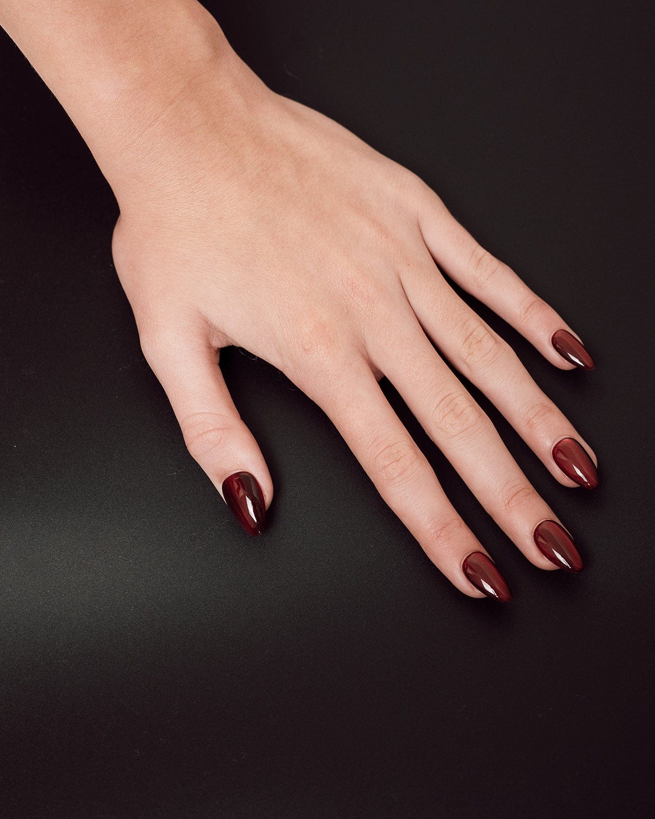 Hand with dark red nail polish on a black background
