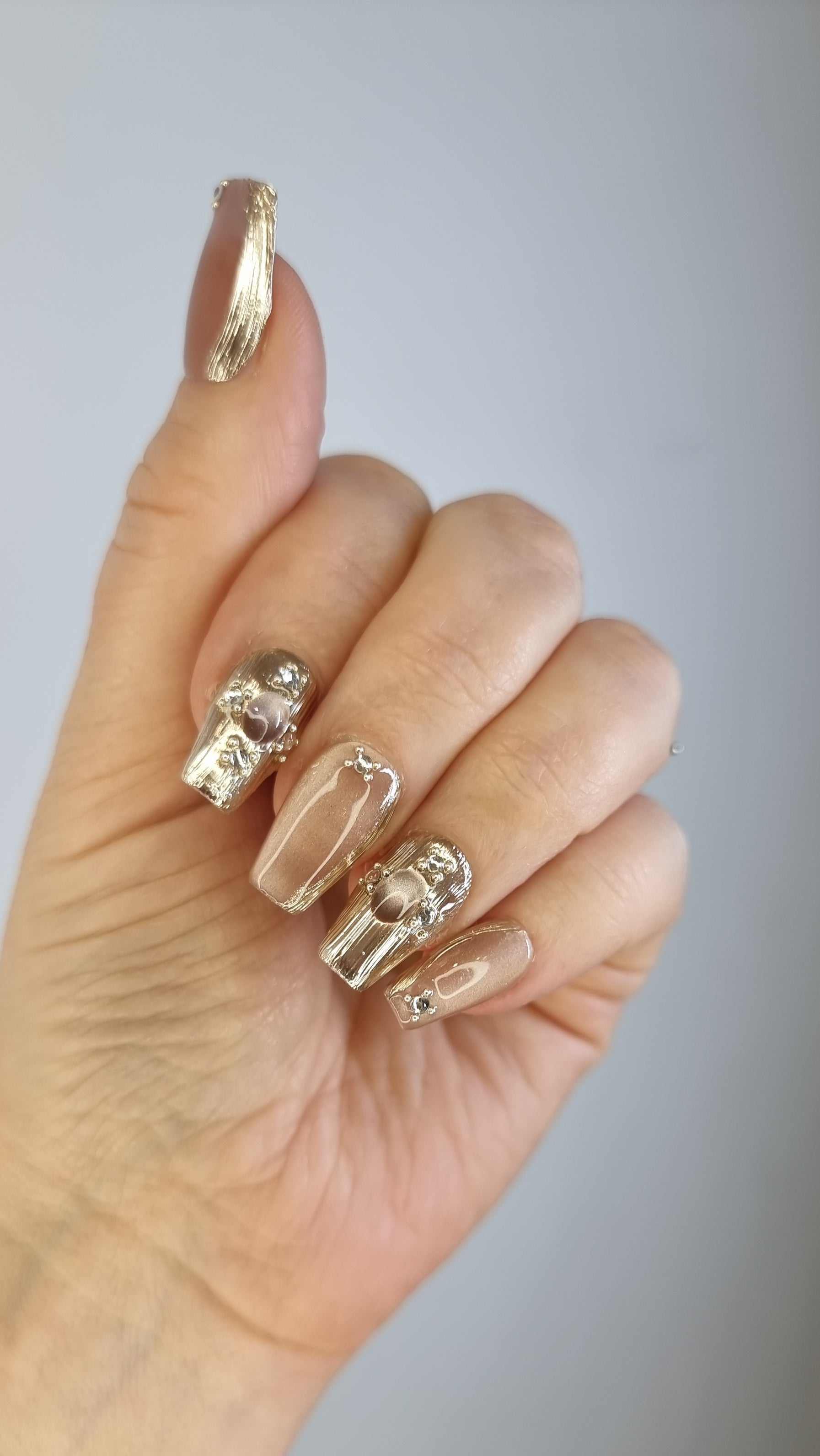 Set of metallic gold, long coffin-shaped Sama press-on nails.