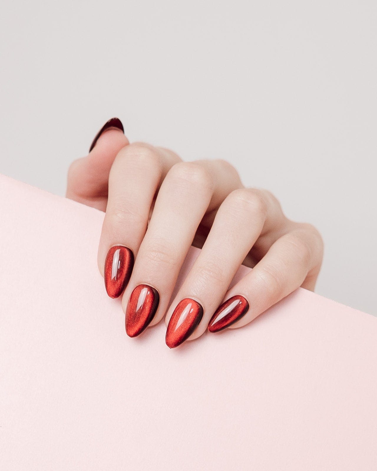 Hand with red nail polish on a light pink background