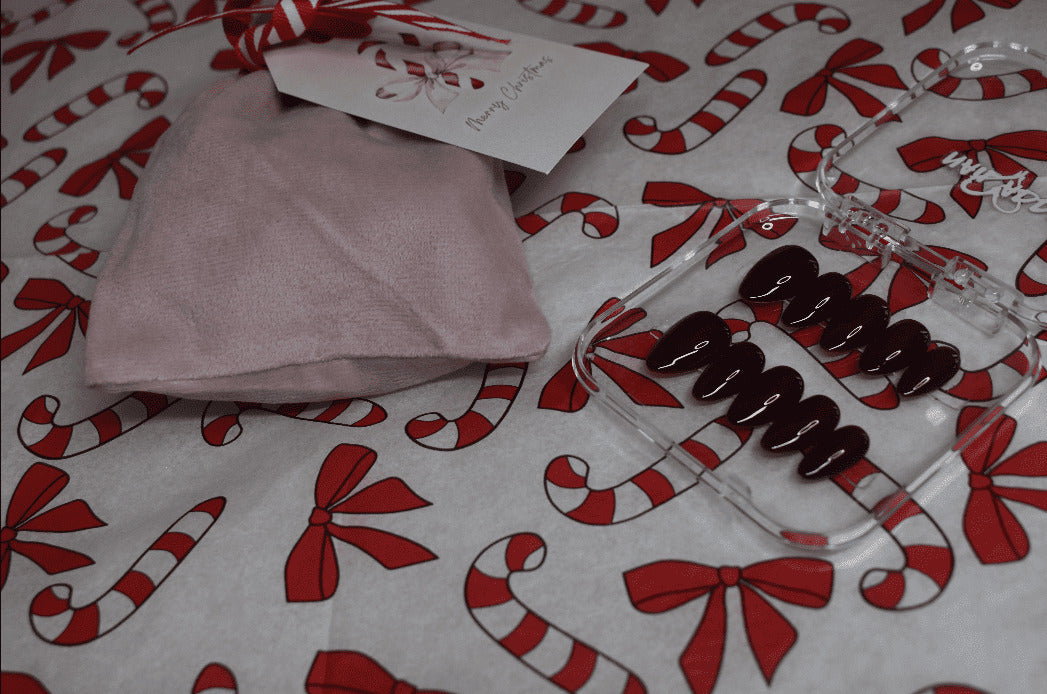 Pink fabric, clear plastic container with brown items, and a card on a candy cane and bow patterned surface.