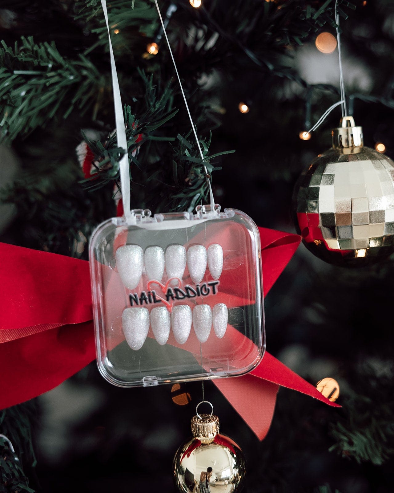 Decorative ornament with white nails in a clear case on a Christmas tree.