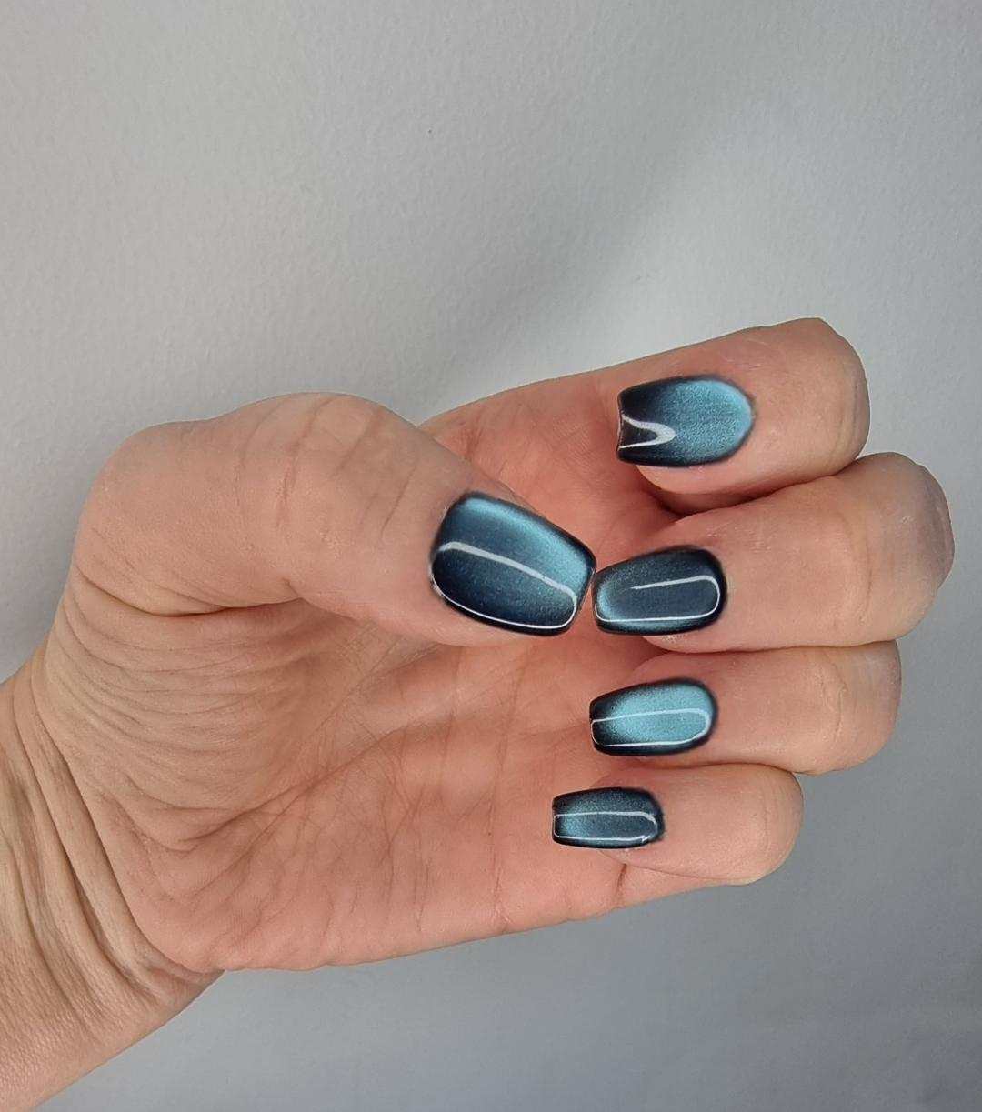 Hand wearing Yalla magnetic press-on nails featuring blue and black shimmering colors.